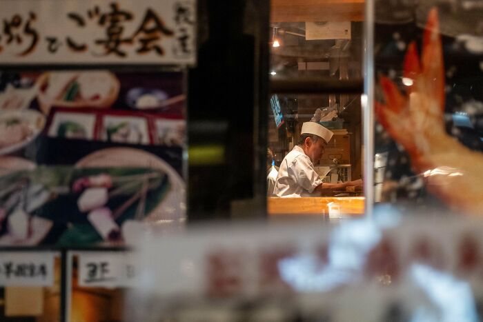 Chef in a kitchen captured through a restaurant window, showcasing creative street photography style.