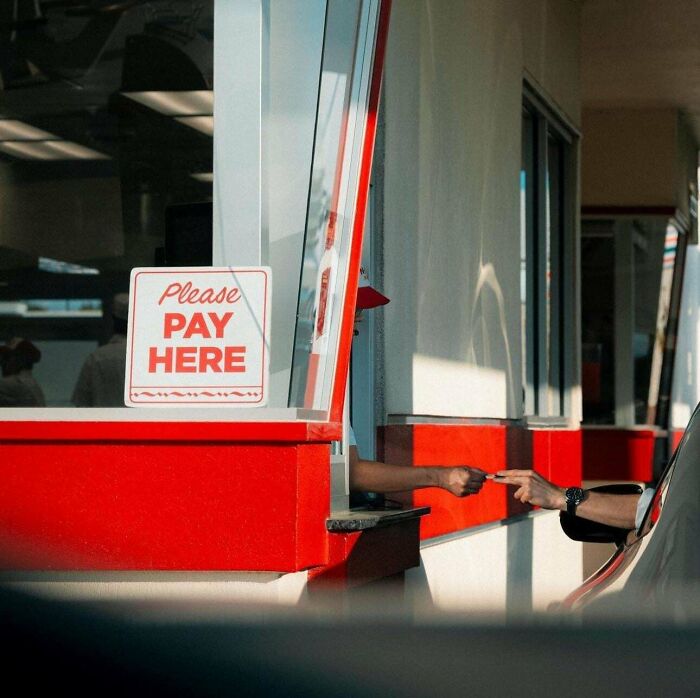 Drive-thru payment, capturing a creative-street-photography moment with hands exchanging money at a pay window.