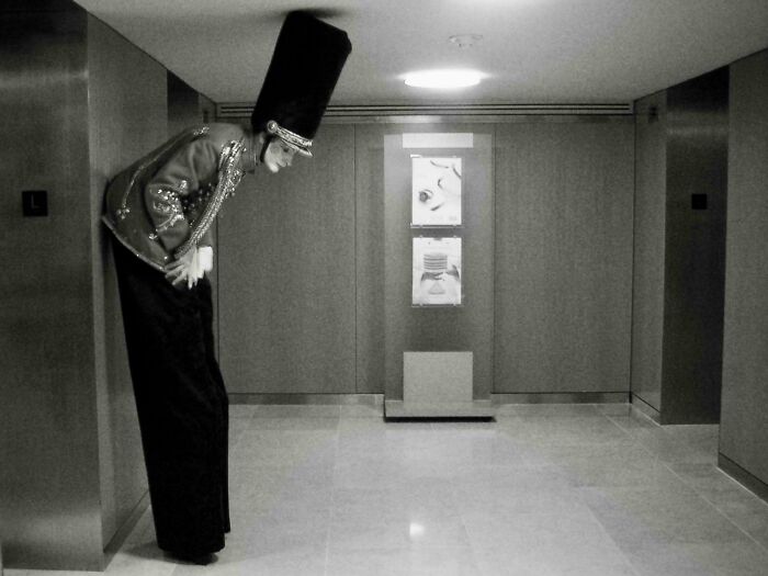 Tall figure in costume leaning in a narrow hallway, captured in creative street photography style.