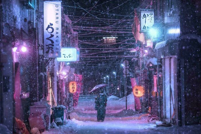 A person with an umbrella walks through a snowy, neon-lit street at night, capturing the essence of creative street photography.