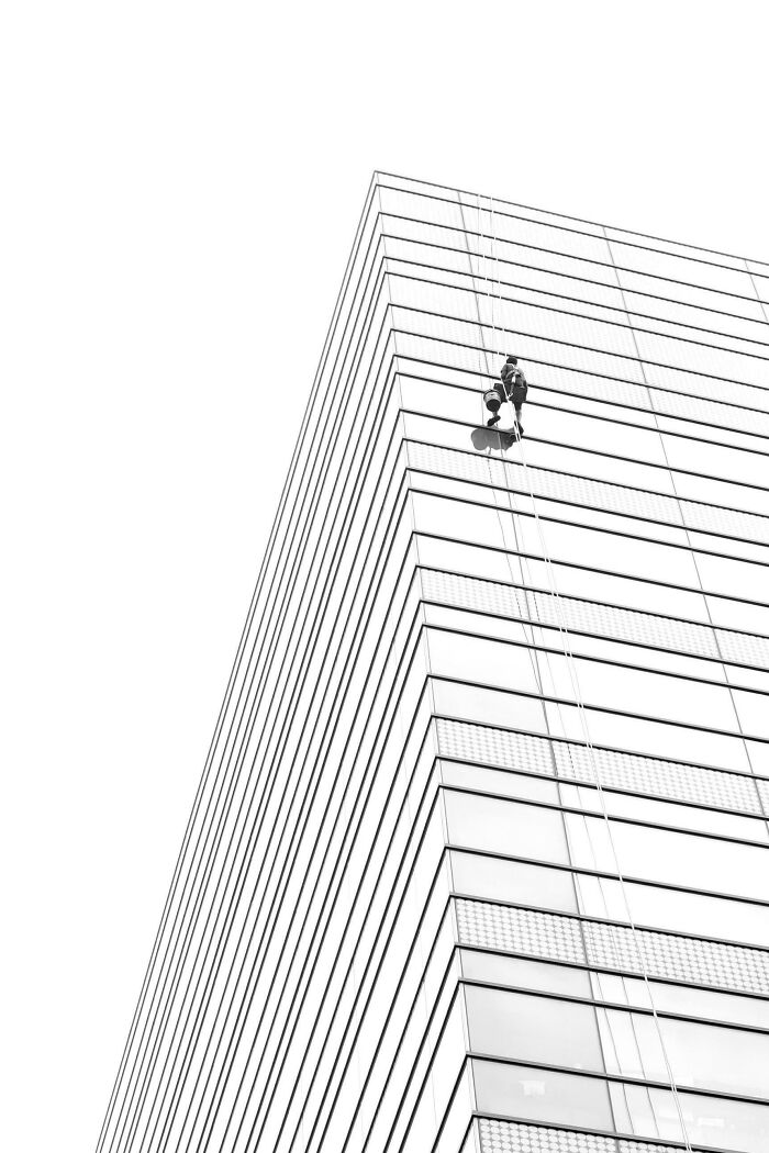 Creative street photography of a window cleaner descending a modern building on ropes.