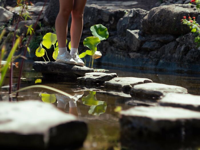 Person stepping on stones across a pond, showcasing creative street photography.