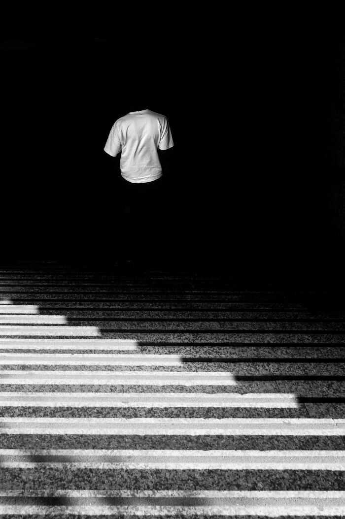 A person in a white shirt stands in shadowy light, exemplifying creative street photography.