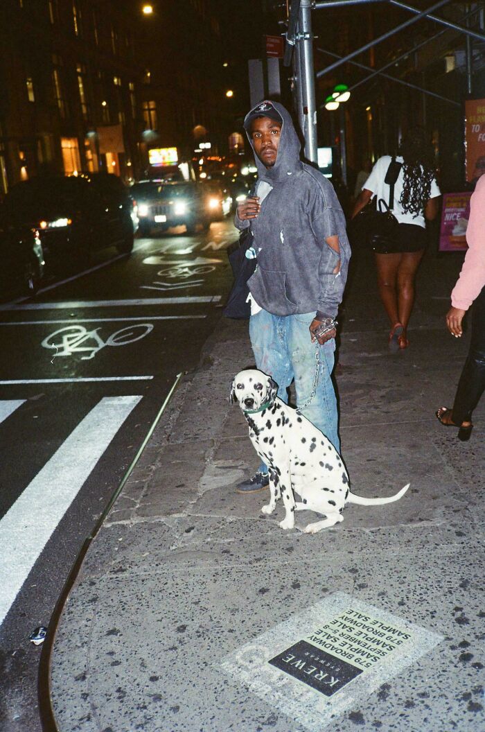 Man in a hoodie with a Dalmatian at night on a city sidewalk, exemplifying creative street photography.