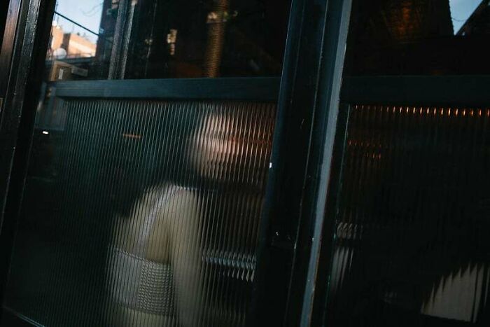 Blurry figure behind a textured glass window, capturing a moody urban scene in creative street photography.