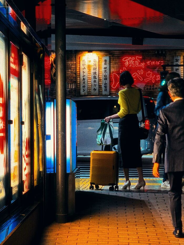 Woman with yellow suitcase in urban night scene, showcasing creative street photography.