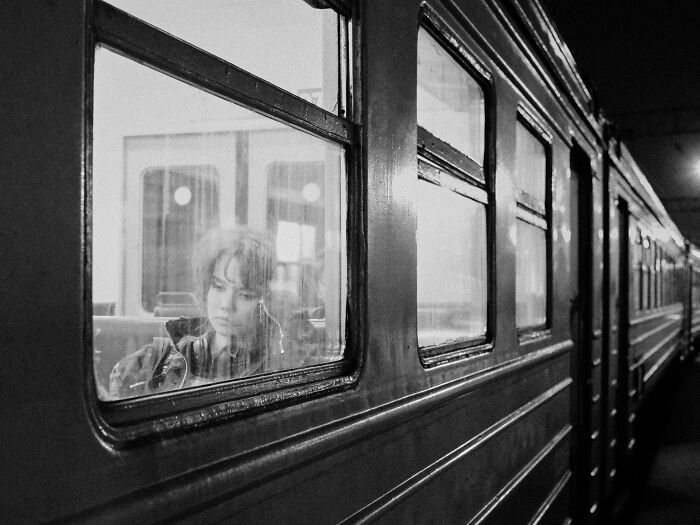 Moody black and white creative street photography of a woman gazing out from a train window at night.