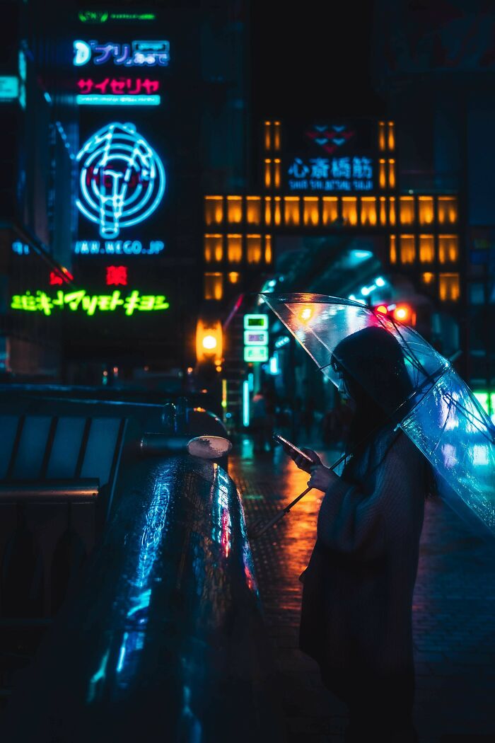 Person under an umbrella, using a smartphone at night, surrounded by neon lights. Creative-Street-Photography.