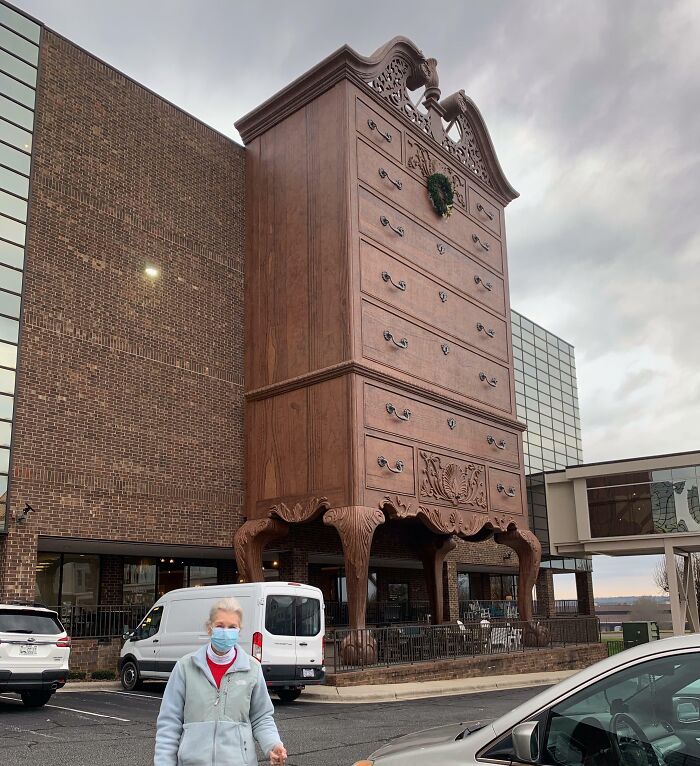 Giant chest of drawers outside a building, a fascinating sight, with a person in the foreground wearing a mask.