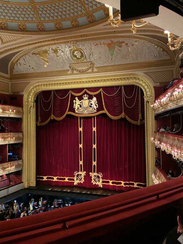 Elegant theater stage with closed red curtains decorated in gold, viewed from the balcony during a Christmas performance.