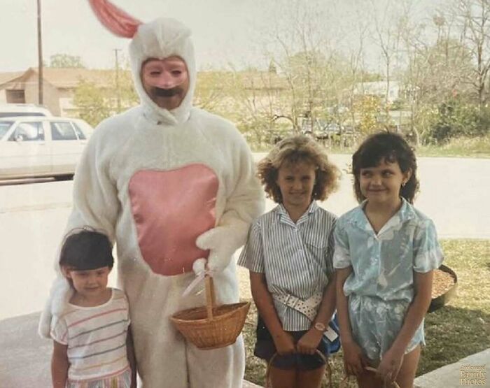 Awkward family photo of a person in a bunny costume with three kids holding baskets outdoors.