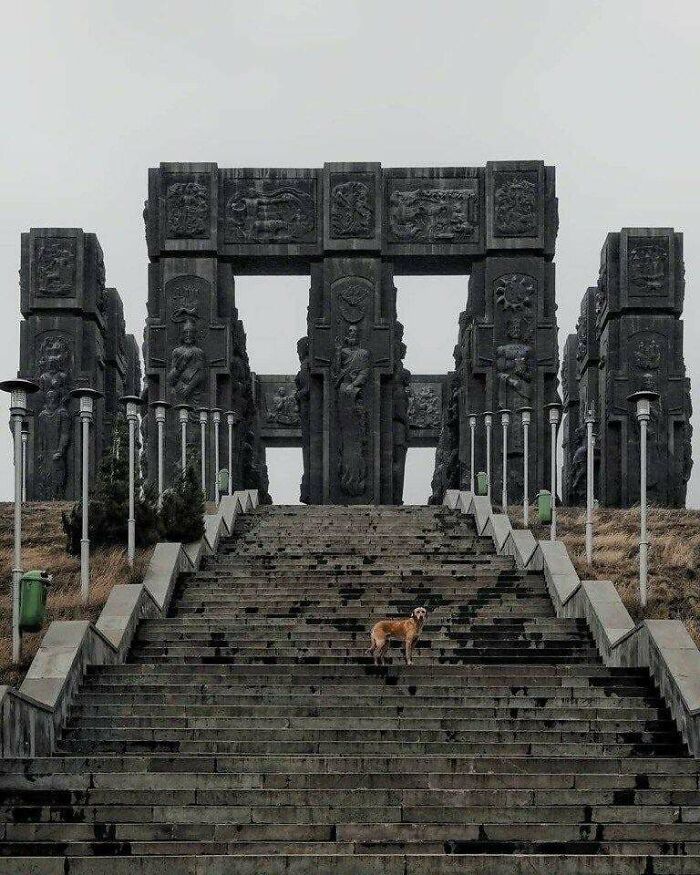A dog stands on stone steps leading to a monumental structure, illustrating urban hell.