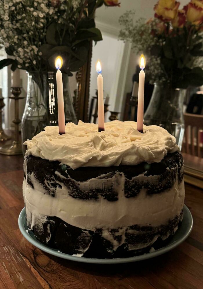Three candles on a rustic chocolate cake with white frosting, showcasing unique baker creativity.