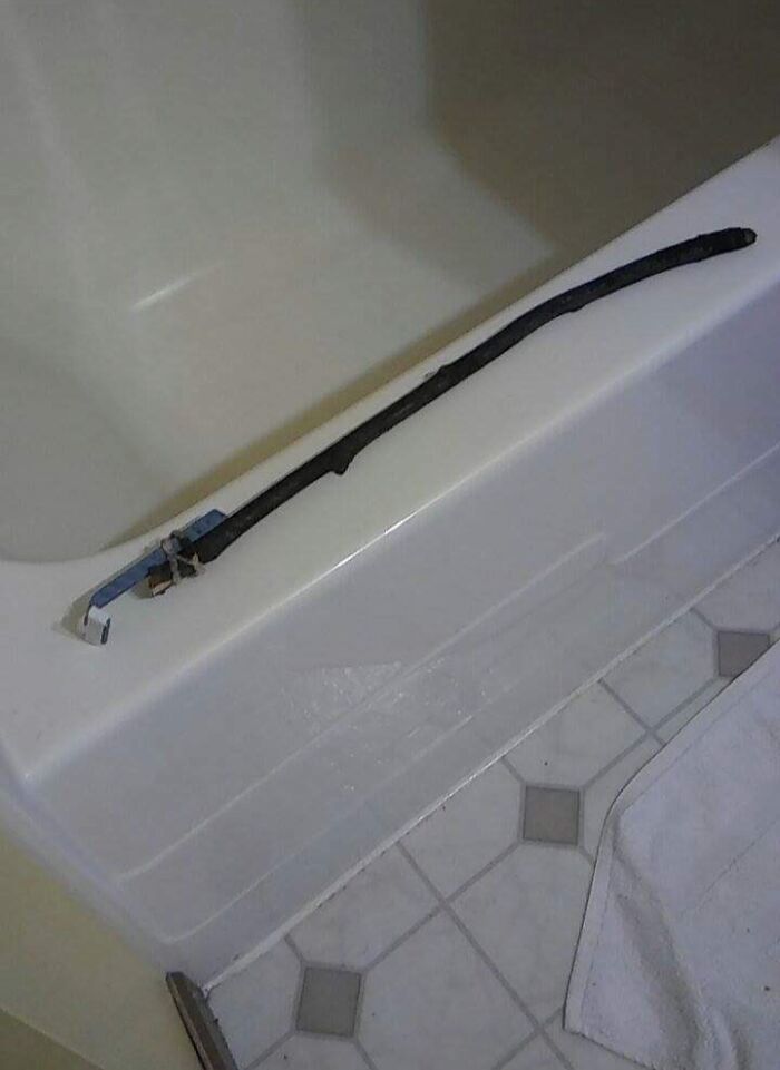 A long black object resembling a belly lounging humorously on a bathtub ledge.