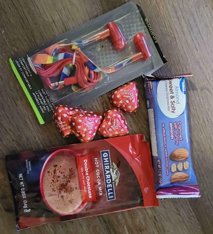 Disappointing presents including colorful earbuds, red chocolates, granola bar, and hot cocoa mix on a wooden surface.