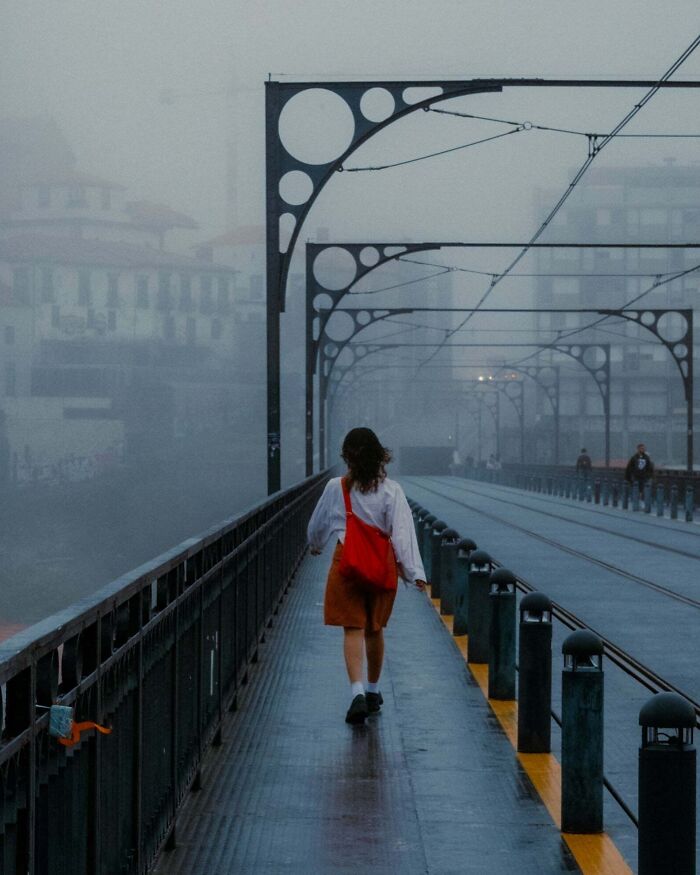 Woman in red bag walking on a foggy bridge, captured in creative street photography.