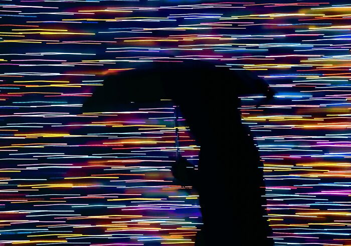 Silhouette of a person with an umbrella against a colorful light streaks background, showcasing creative street photography.