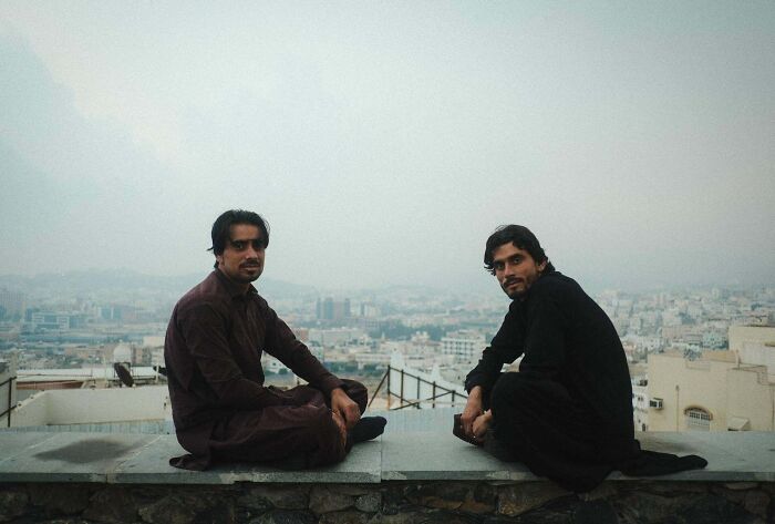 Two men sit on a rooftop ledge with a cityscape view, exemplifying creative street photography.