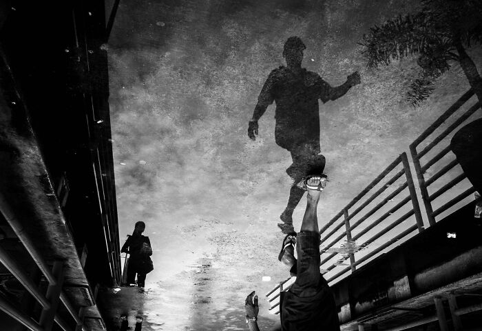 Reflected shadows of people walking on wet street, showcasing creative-street-photography in black and white.