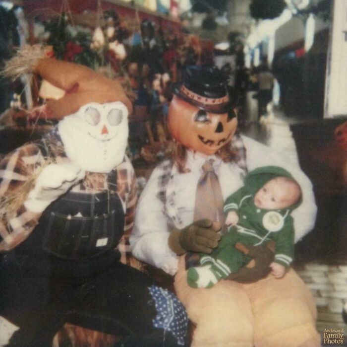 Awkward family photo of two costumed figures with a baby.
