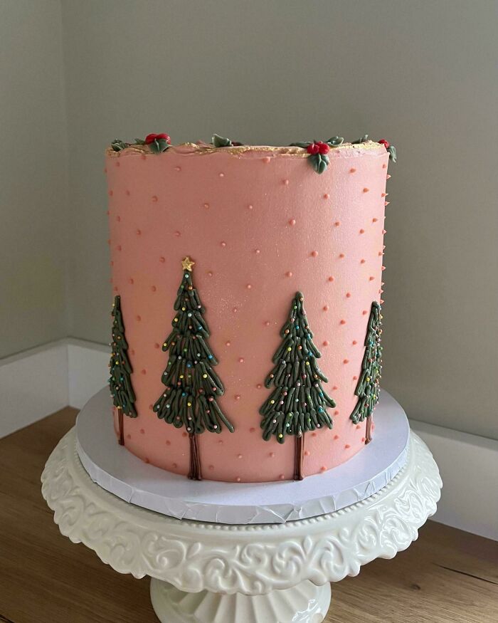 A tall, intricately decorated pink cake with Christmas trees, showcasing a baker's elevated culinary artistry.
