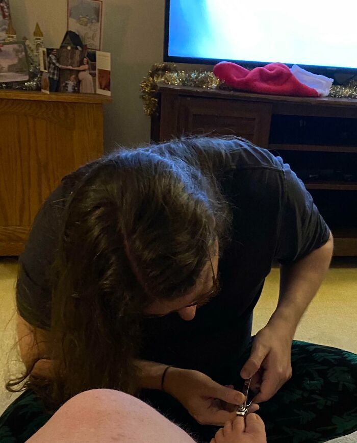 Person trimming toenails, humorous pregnancy situation in a cozy living room.