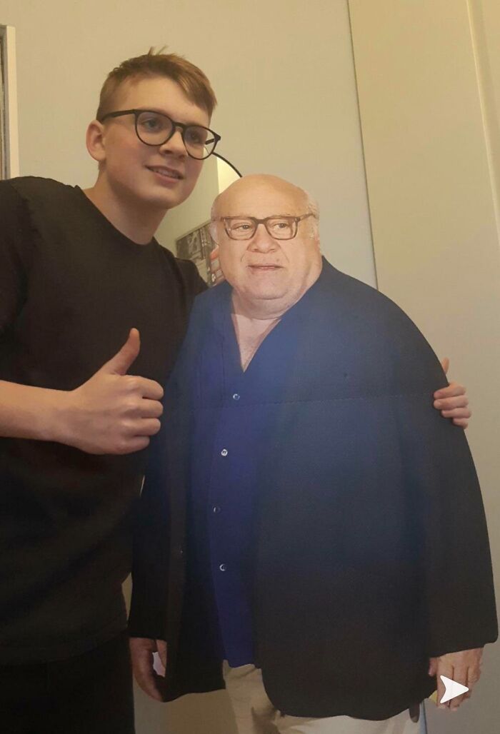 Teen boy smiling next to a Danny DeVito cutout, showcasing hilarious trolling Christmas gifts.