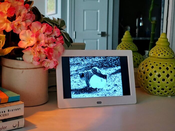 Digital photo frame on table with flowers and decorative items, a perfect Christmas gift for making moms cry happy tears.