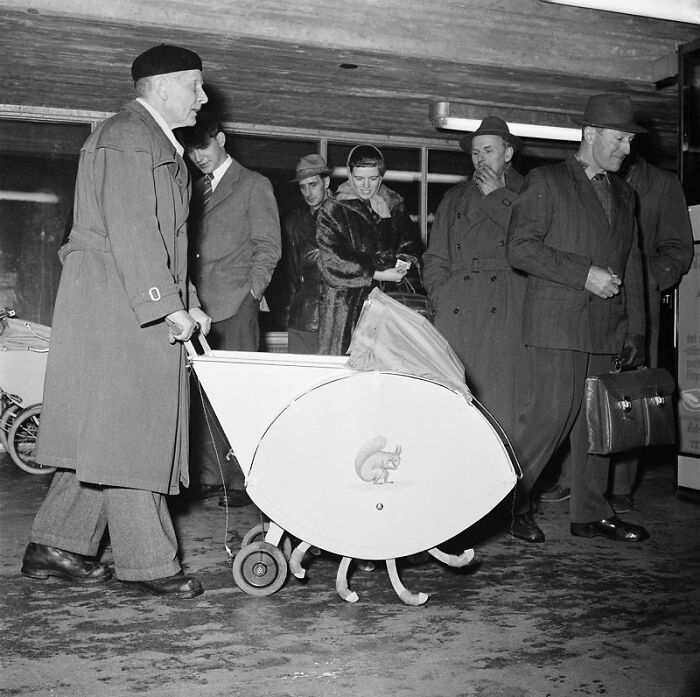 Man pushing unique stroller, an example of strange inventions, surrounded by onlookers in coats and hats.