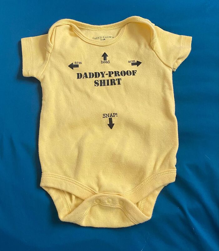 Yellow onesie labeled "Daddy-Proof Shirt" with arrows, highlighting disappointing gifts theme.