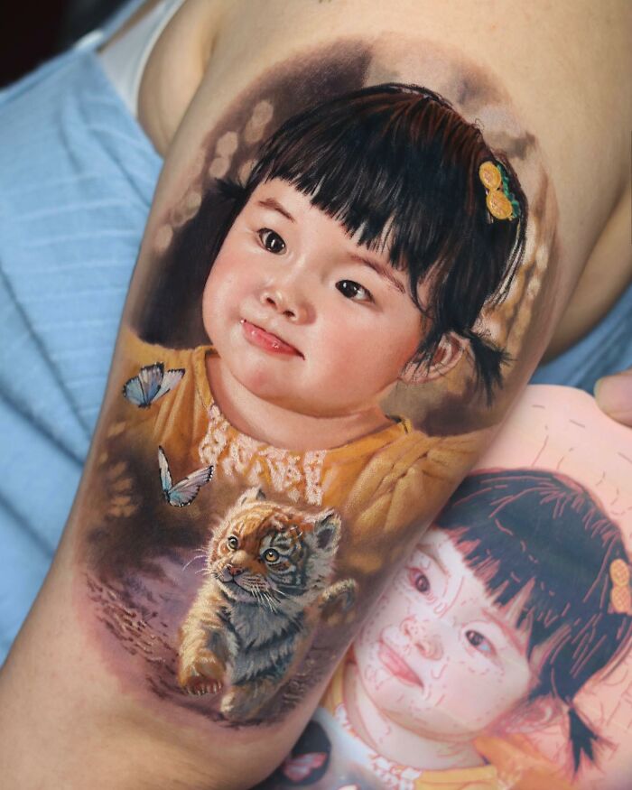 Realistic tattoo of a child with butterflies and a tiger cub, showcasing mastery in tattoo art.