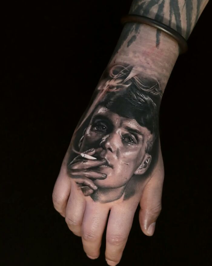 Realistic tattoo art of a person's face on a hand, showcasing mastery of realism and illusion in ink.