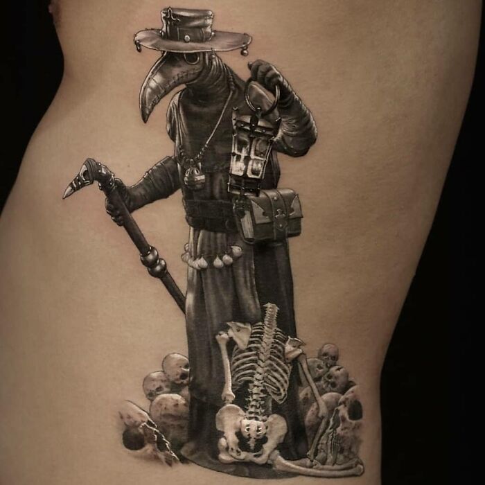 Realism in tattoo art depicting a plague doctor and skeleton, showcasing intricate details and shading on skin.