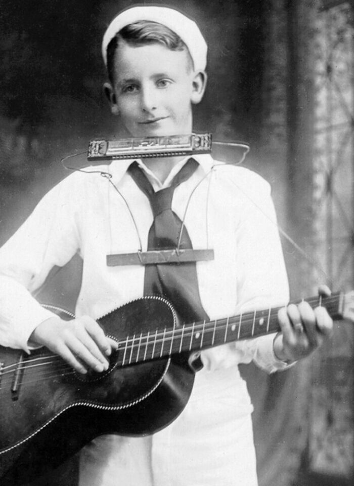 A boy playing guitar with a harmonica holder, showcasing strange inventions.