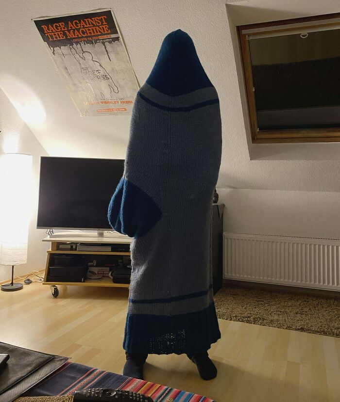 Person humorously wrapped in a giant sock, standing in a living room, embodying a funny Christmas gift prank.