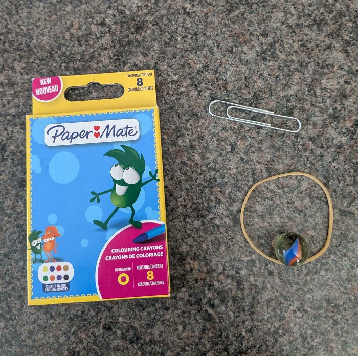 Crayons box, paperclip, rubber band, and marble on a countertop, illustrating disappointing presents.