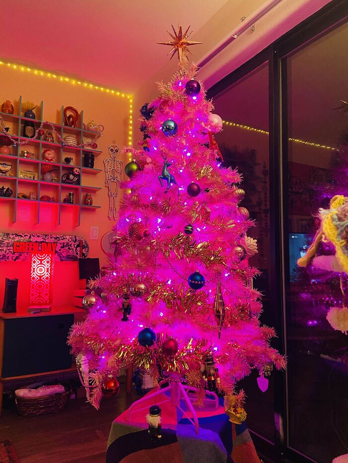 Pink-lit Christmas tree adorned with colorful ornaments in a cozy room.