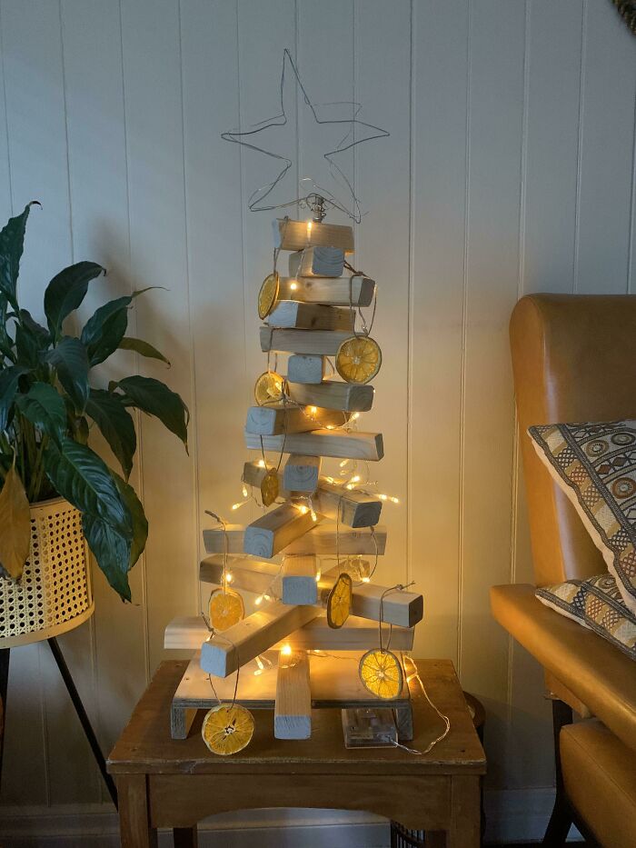 Creative Christmas tree idea with stacked wood blocks, citrus slice ornaments, and glowing lights on a side table.
