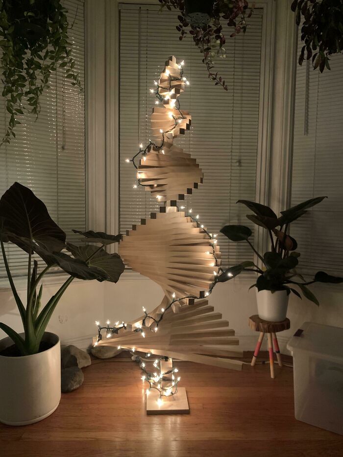 Wooden spiral Christmas tree idea with string lights, surrounded by potted plants in a cozy room.