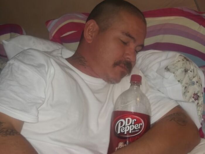 Man asleep, hugging a Dr. Pepper bottle, showcasing a funny scene from social media.