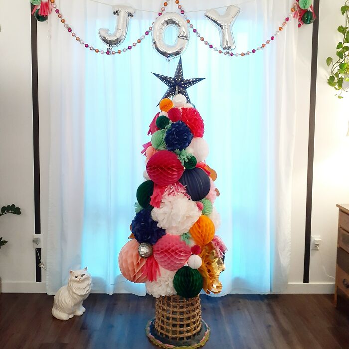 Colorful Christmas tree made of paper decorations with "JOY" balloons above.
