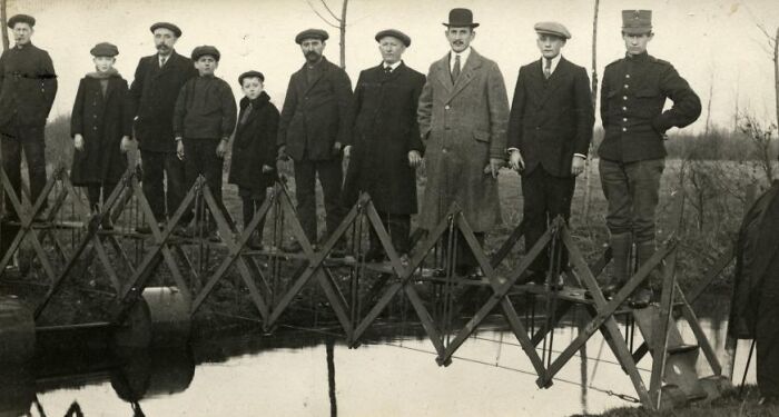 People standing on a strange accordion-style bridge over a small stream, showcasing an unusual invention.