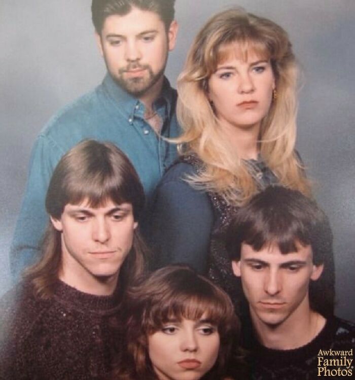 Awkward family photo with five somber adults posing against a gray studio backdrop.