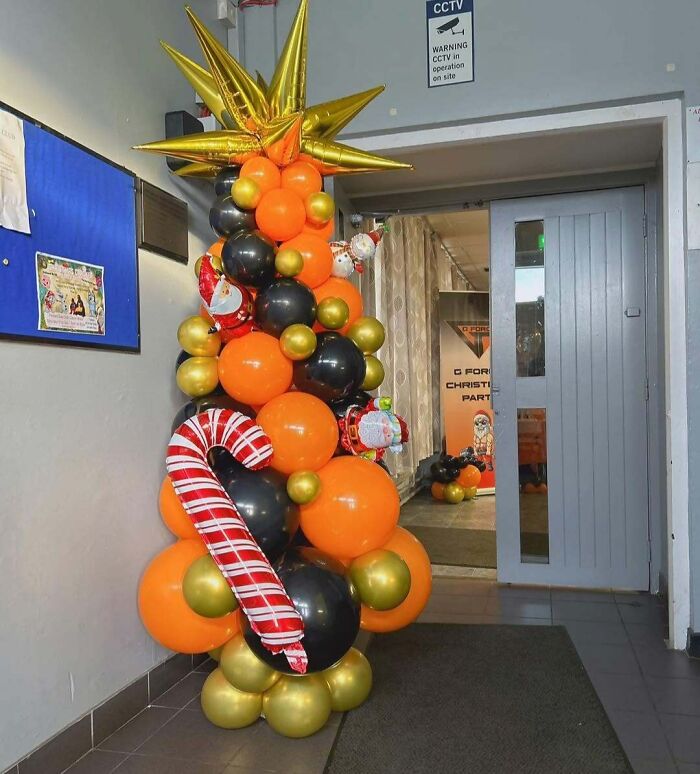 Balloon Christmas tree idea with orange, black, and gold balloons, topped with a shiny star and candy cane decoration.