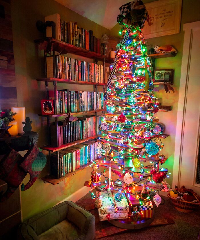 Unique Christmas tree idea with colorful lights and ornaments beside a bookshelf in a cozy room.