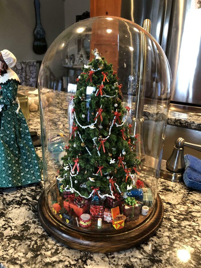 Miniature Christmas tree covered in a glass dome with DIY decorations and presents on a granite countertop.