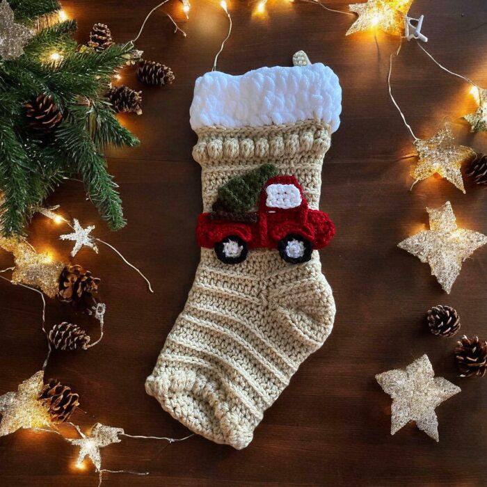 Handmade crochet Christmas stocking with a red truck design, surrounded by festive lights and pine cones.