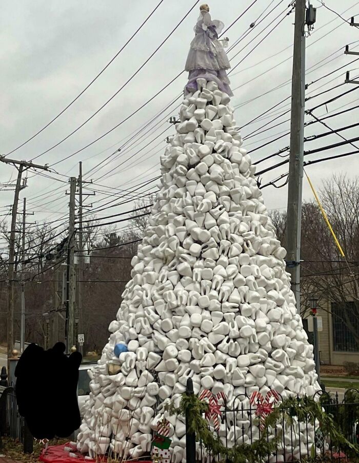 Unique Christmas tree made of stacked white objects with a doll on top, located outdoors with power lines in the background.