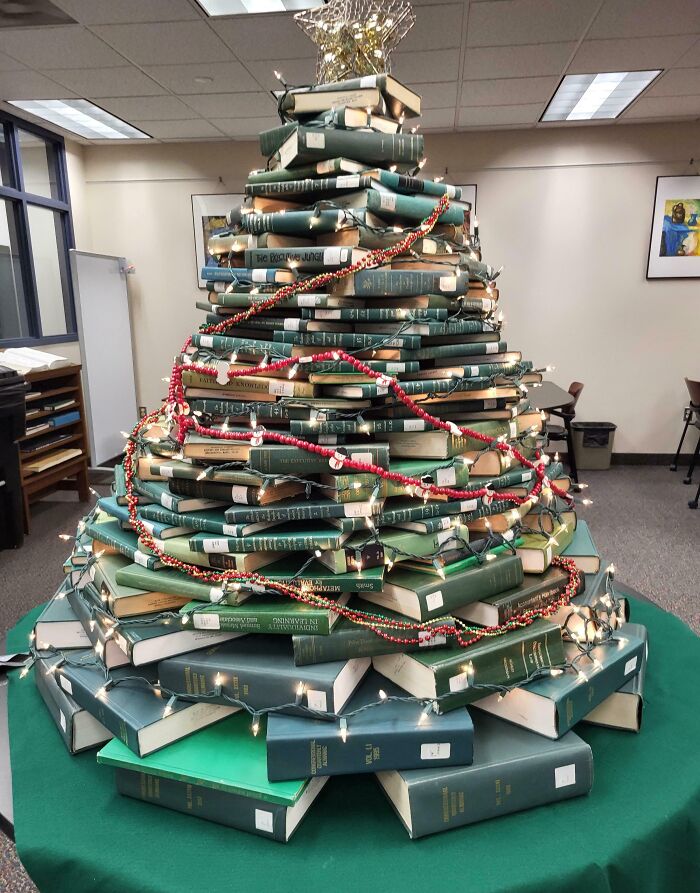 Stacked books forming a Christmas tree, adorned with lights and garlands, showcasing a unique Christmas tree idea.