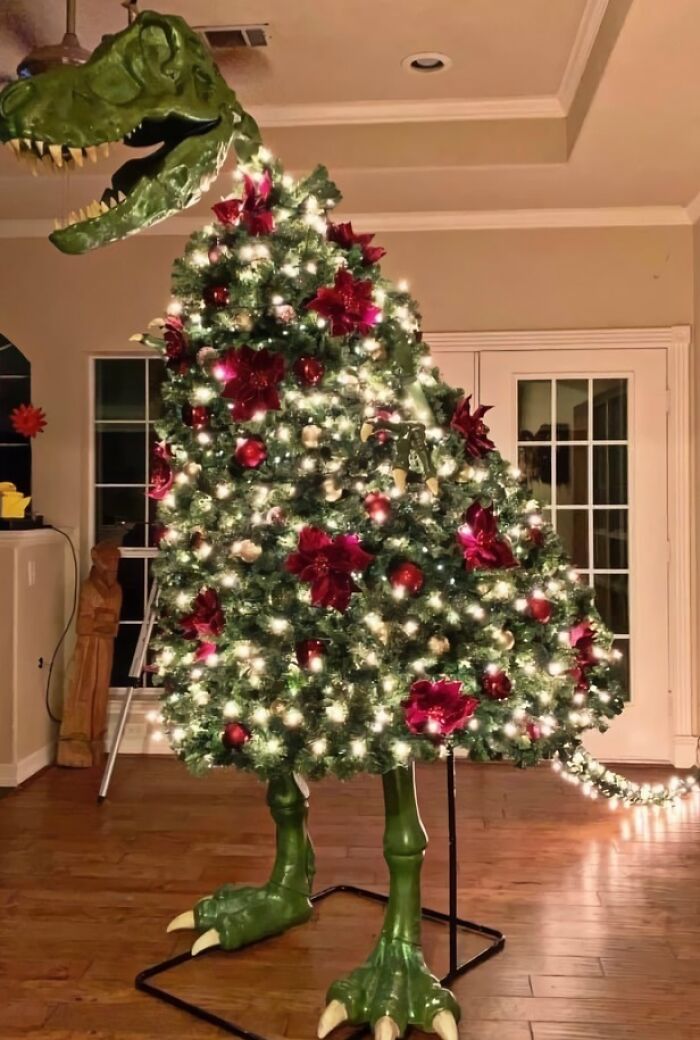 Dinosaur-shaped Christmas tree with lights and red ornaments inside a room.